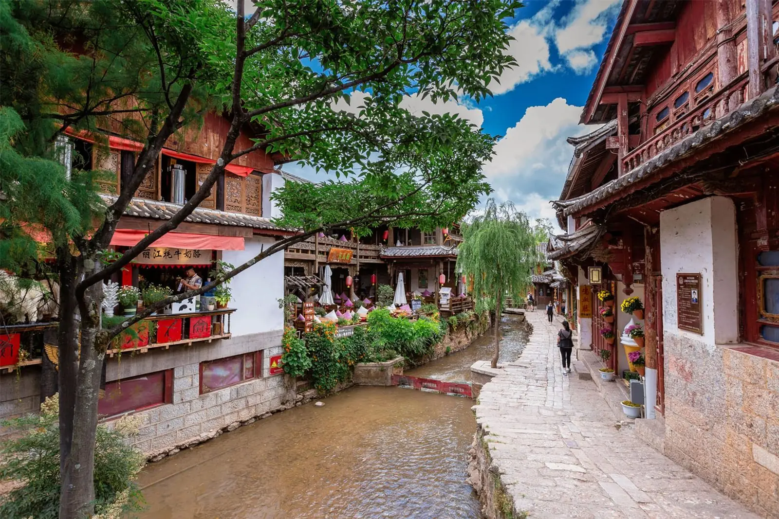 A willow-lined canal and stone street in Lijiang old town in Yunnan, tiled roofs and red lanterns either side